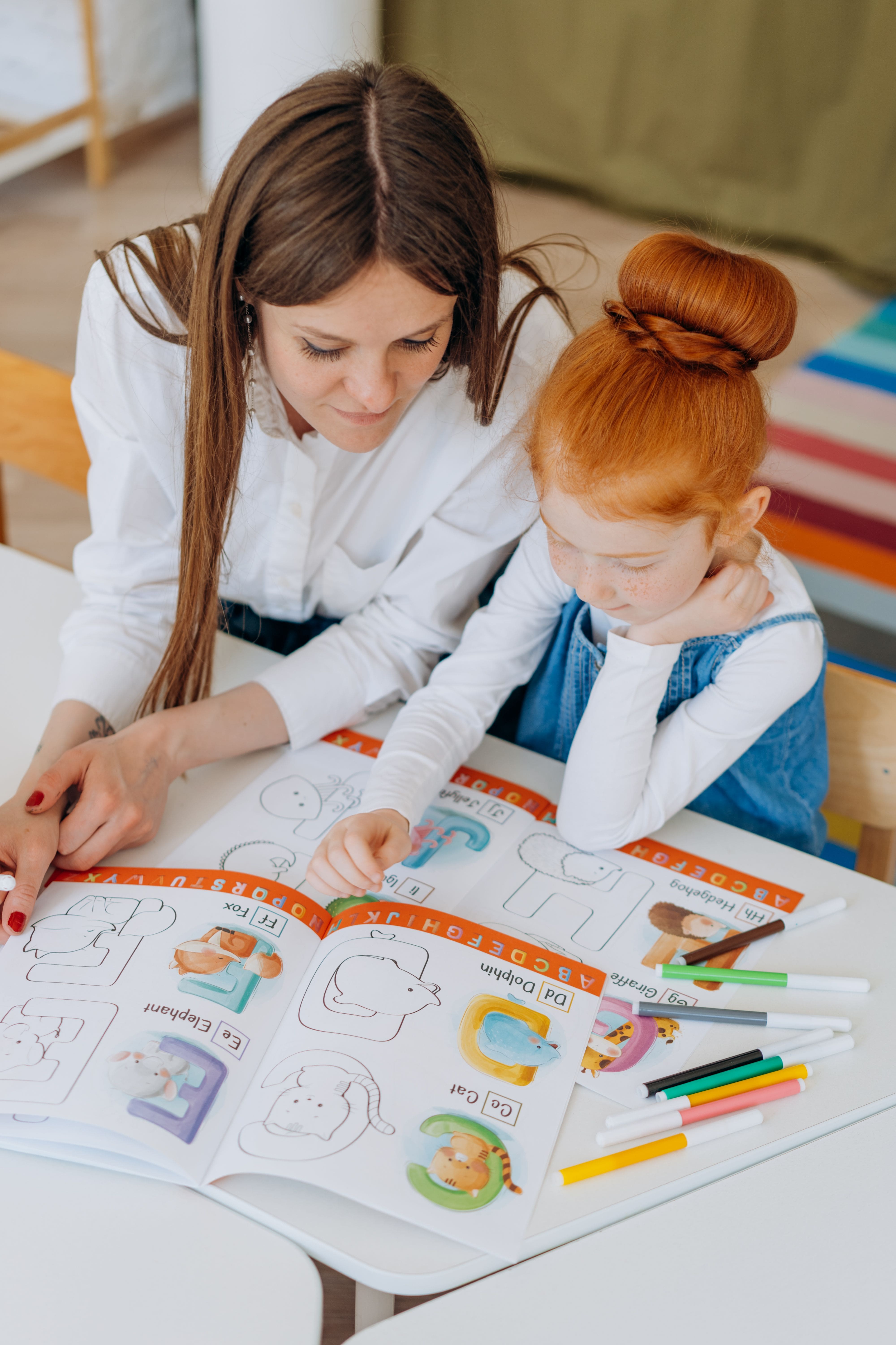 Maestra apoyando a una alumna con actividades de inglés y lectoescritura.